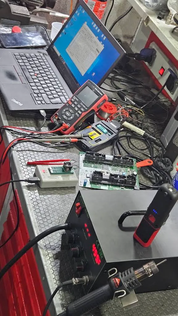 Radni sto u radionici: laptop sa softverom za mape, otvorena upravljačka jedinica motora, programator, multimetar i stanica za lemljenje.